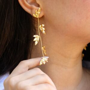 Woman wearing gold leaf-designed jewelry earring, holding it gently with her fingers.